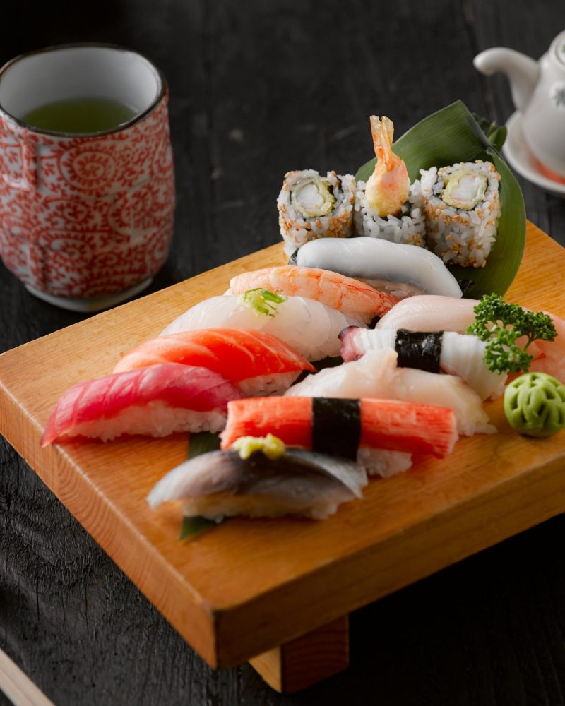 Elegant display of sushi with green tea on a wooden board, capturing authentic Japanese cuisine.
